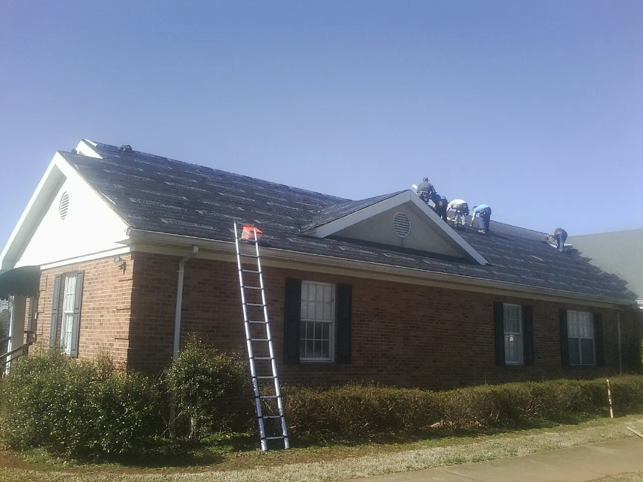 Crew tearing shingles off a brick ranch roof with a ladder set — Emergency Roof Repair work by our crew in Bethlehem