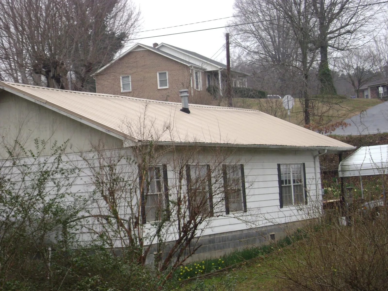 Tan metal roof on a white sided house set into a hillside — Commercial Roofing by Roofing Brothers in Bethlehem